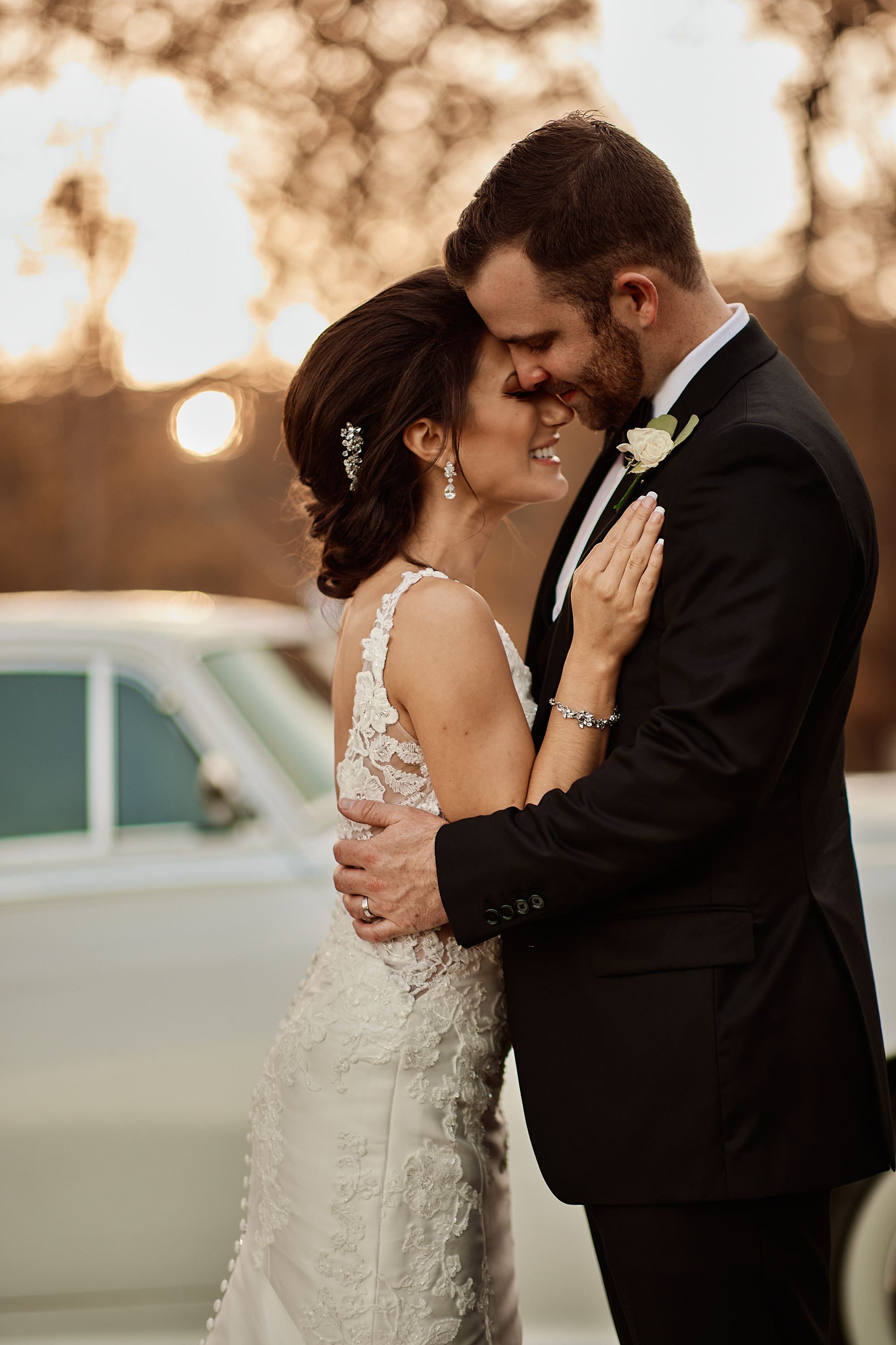Close up portrait of a bride and groom embracing by a classic car